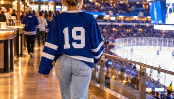Hockey jersey outfit: woman seen from behind on an arena concourse in an oversized blue jersey, light jeans and white chunky sneakers