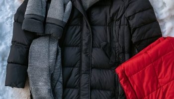 Hockey mom outfits flat lay with a long black puffer coat, cream knit beanie, mittens, coffee tumbler and warm boots