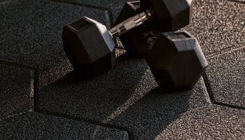 Black interlocking rubber floor tiles with a pair of hex dumbbells resting on them