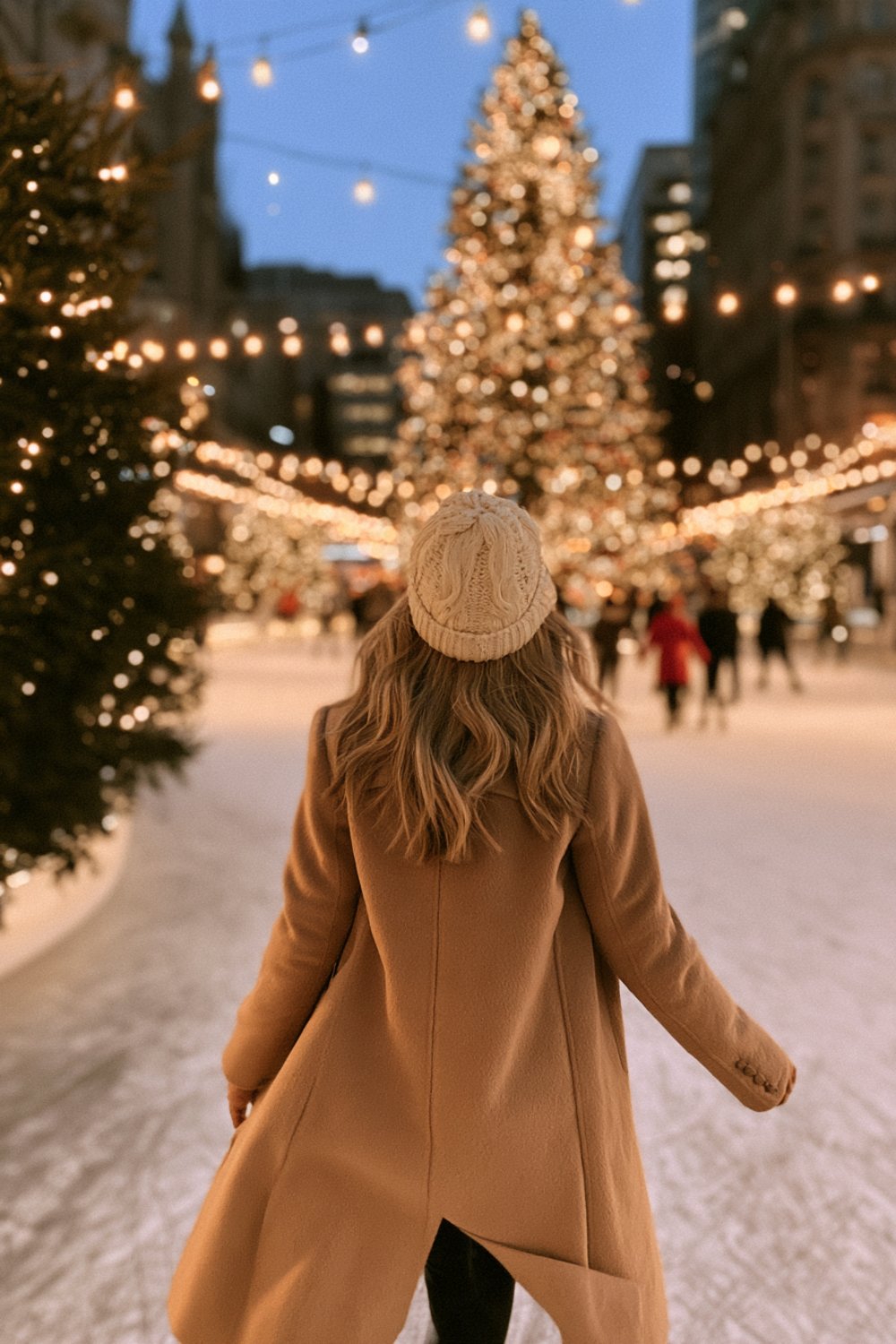Skater seen from behind on an outdoor rink at dusk in a camel wool coat and cream knit hat, lit trees around