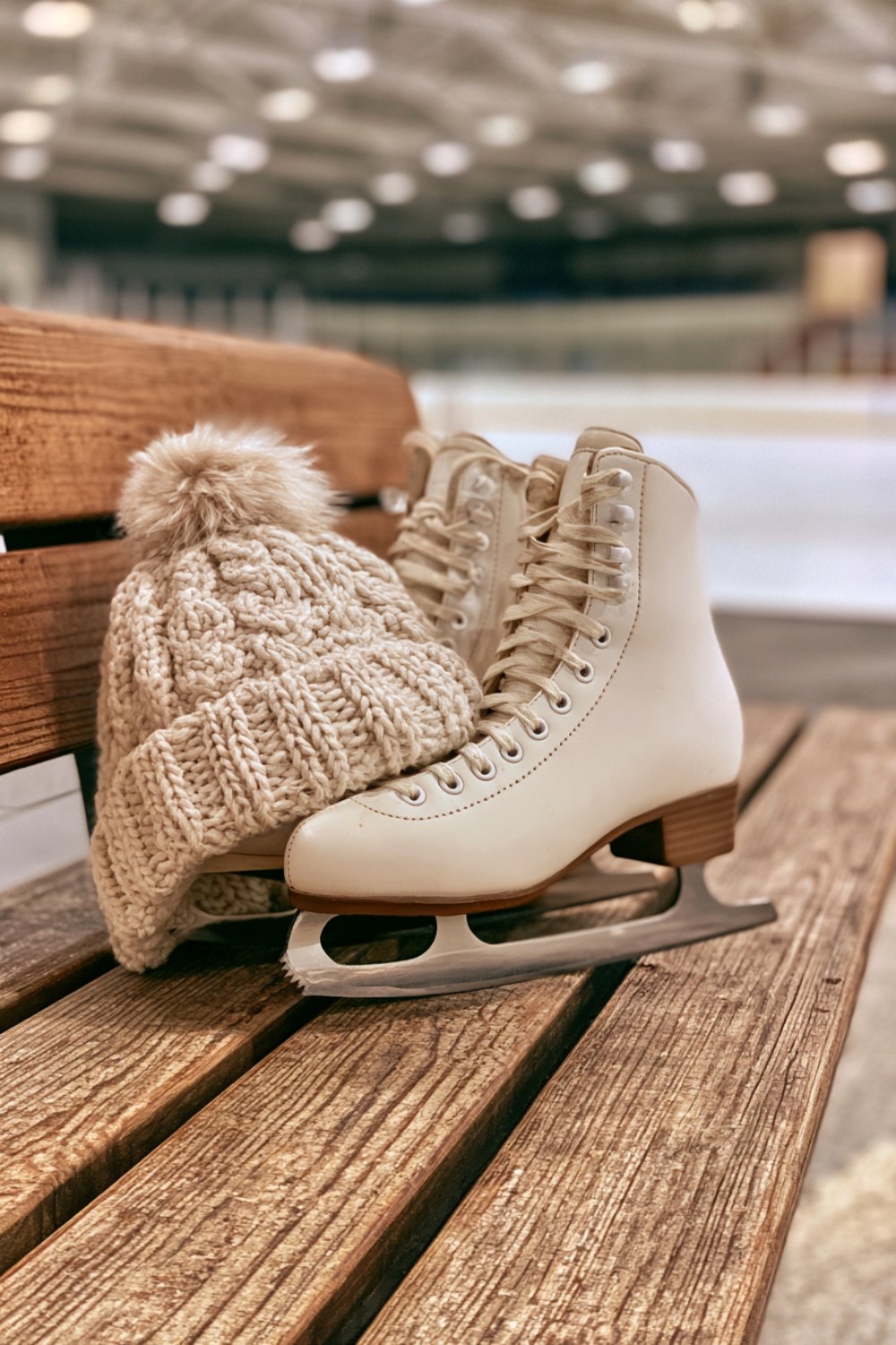 Ice skates with blade guards and a knit hat on a bench beside an indoor rink