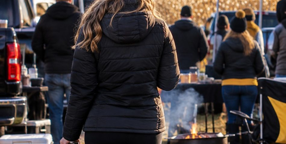 Woman seen from behind at a Midwest tailgate in a black puffer jacket and gold knit beanie