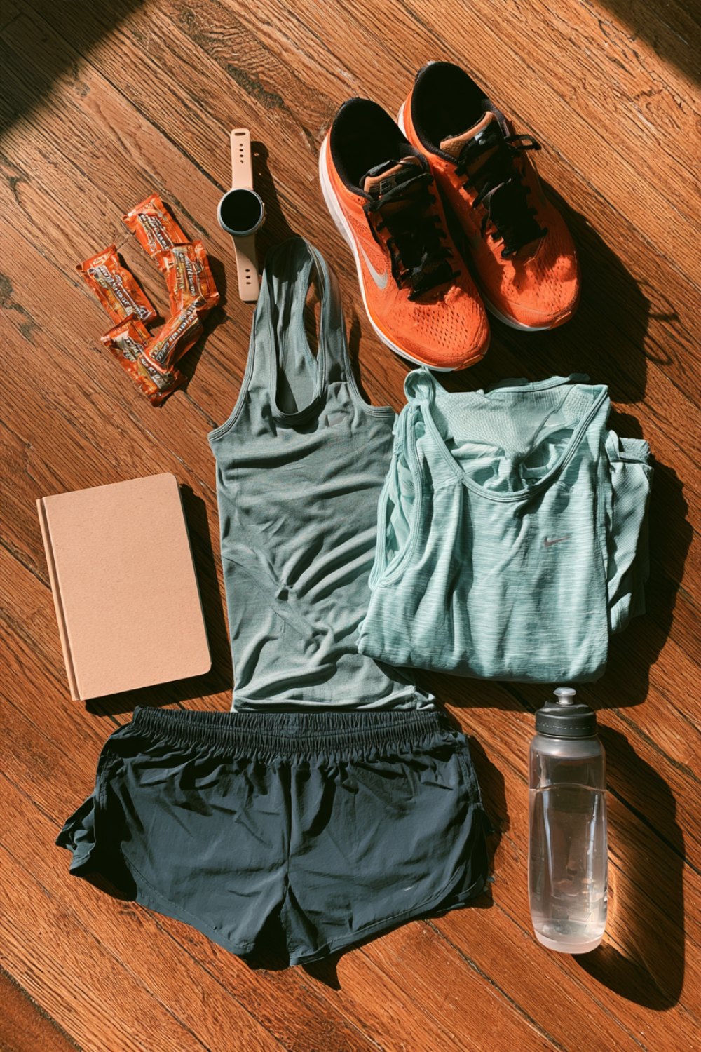 Long run kit on a wooden floor with gels, a notebook, shorts and running shoes