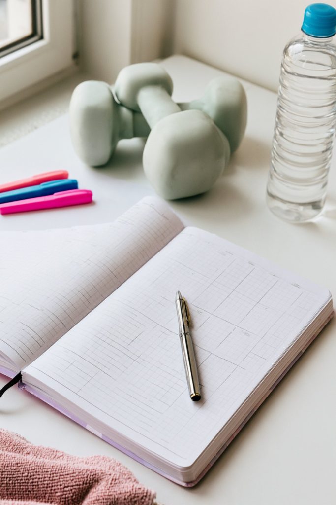 Open blank workout log with a pen beside a pair of small dumbbells