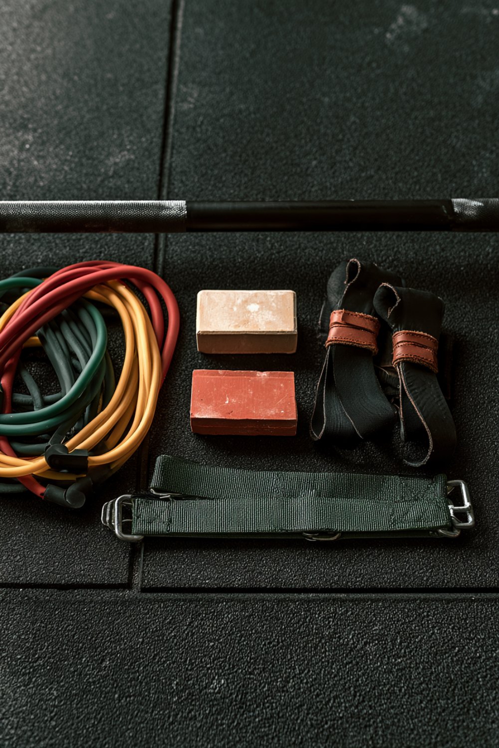 Resistance bands, lifting chalk and grips laid out on black rubber gym flooring