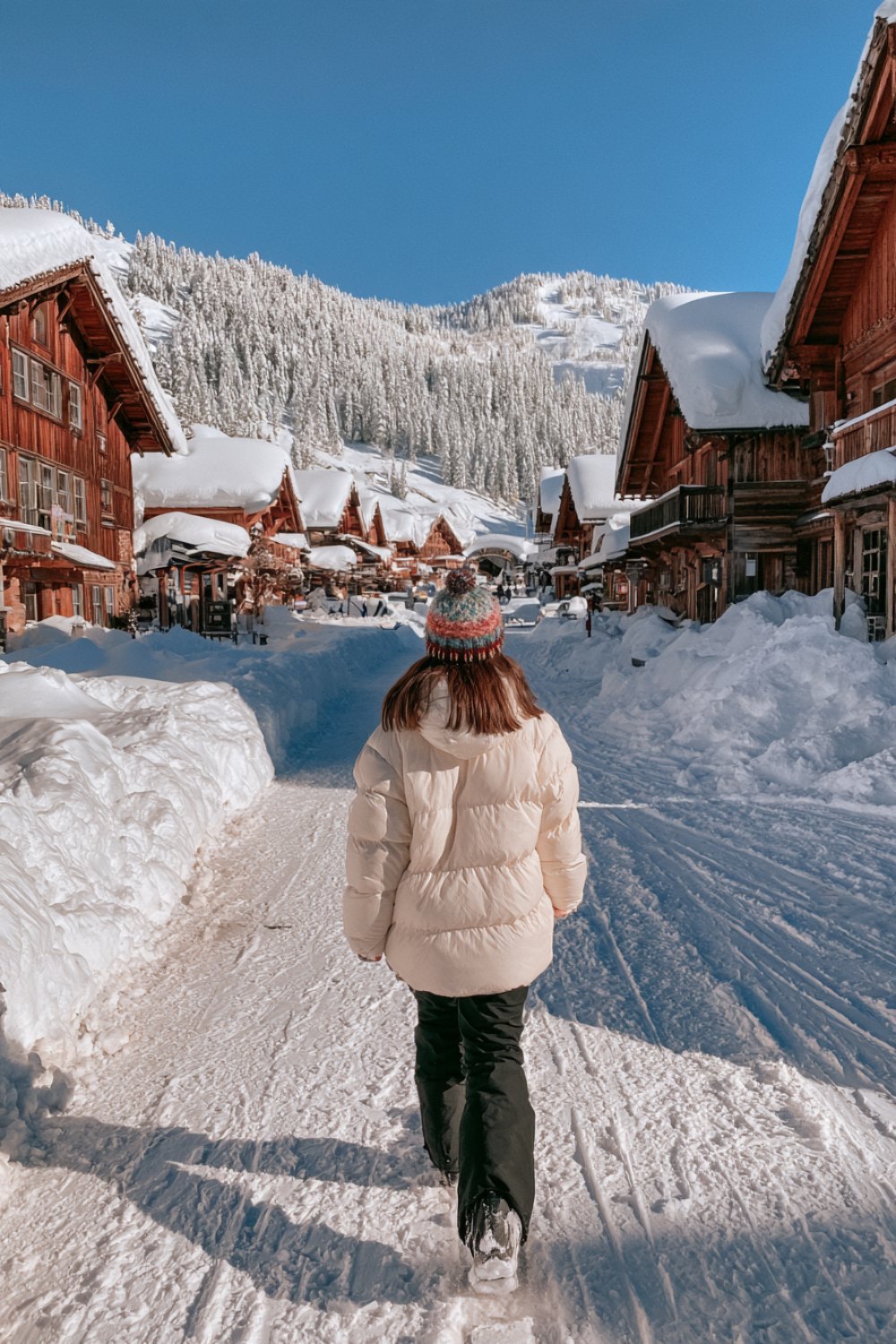 Cream puffer, beanie and black snow pants on a snowy chalet street seen from behind