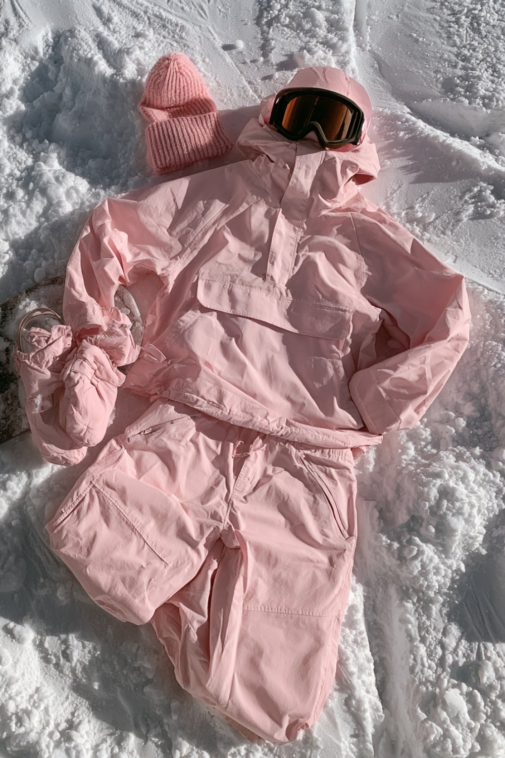 Pastel pink baggy snowboarding outfit with goggles laid out on snow