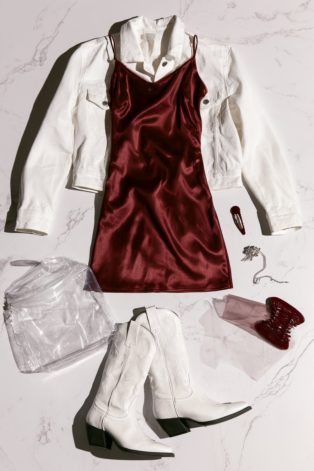 Texas A&M game day outfits flat lay with a maroon satin slip dress, white denim jacket, white western boots and a clear bag