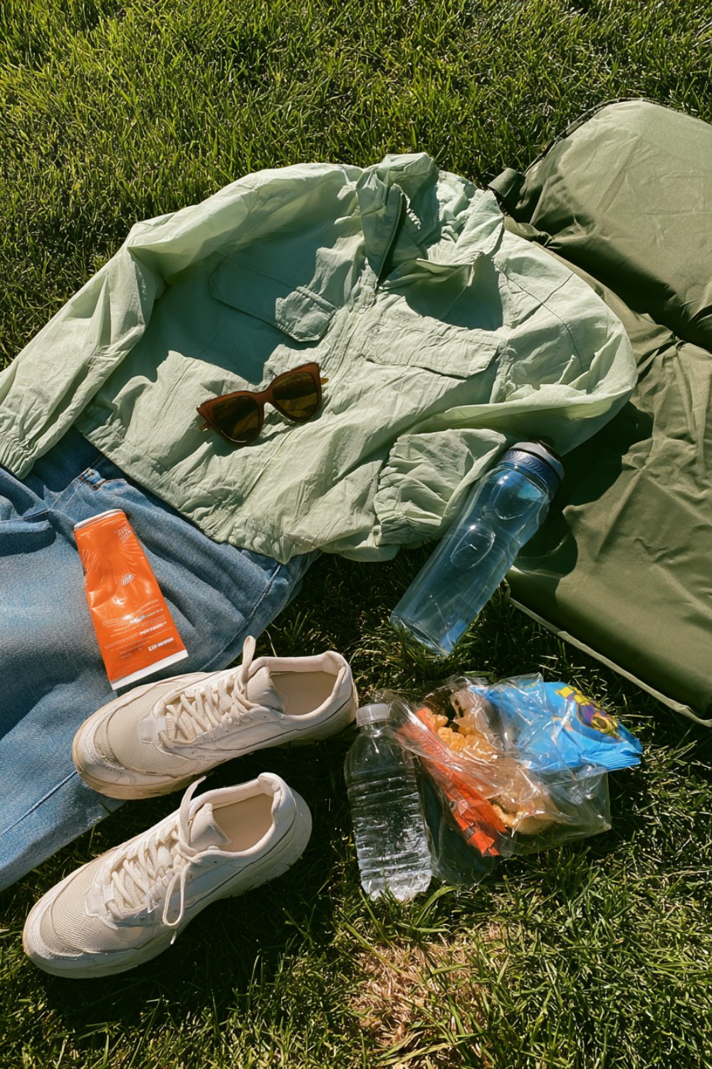 Mint jacket, jeans, sneakers, water bottle and sunscreen in a track mom outfit flat lay