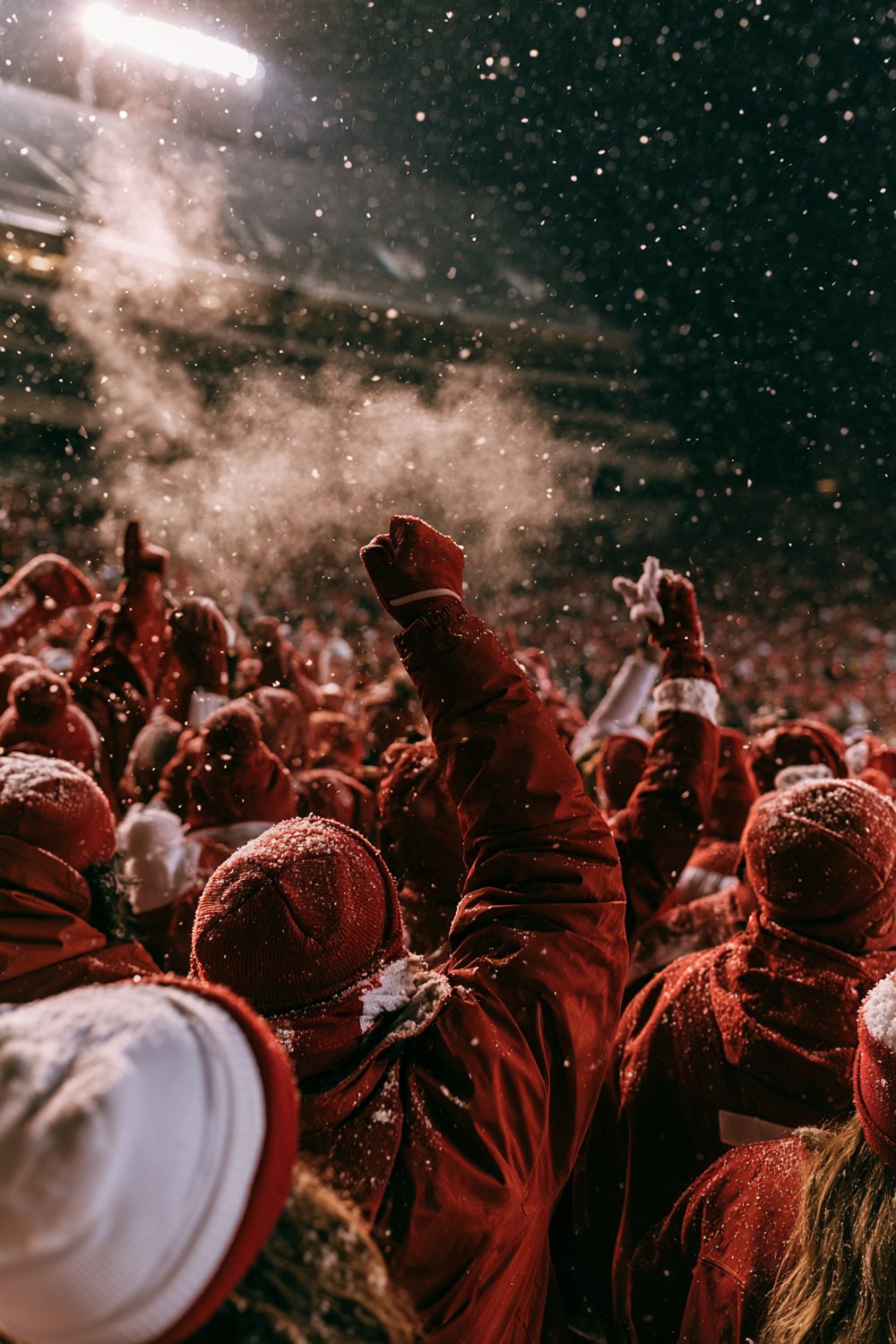Crowd in red and white winter layers seen from behind cheering in a snowy college football stadium, another angle
